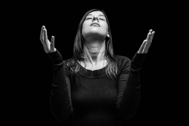 祈っていると、神への崇拝に広げられた腕によって女性を喪閉じた目の頭に、苦しむ、黒の背景に。宗教、信仰、祈り、悲しみのための概念を悼む、痛み、うつ病. - 写真・画像