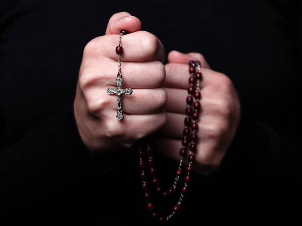 Naisen kädet rukoilee pitämällä rukousnauha Jeesuksen Kristuksen ristillä tai krusifiksi mustalla pohjalla. Nainen, jolla on kristitty katolinen uskonto
 - Valokuva, kuva