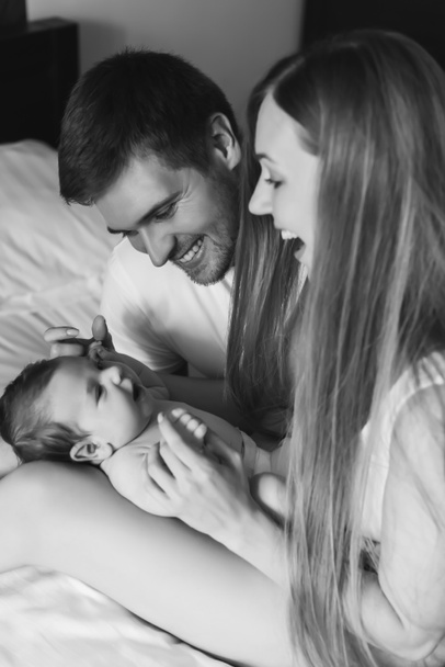 Черно-белая фотография счастливой семьи, играющей с младенцем в постели дома
 - Фото, изображение