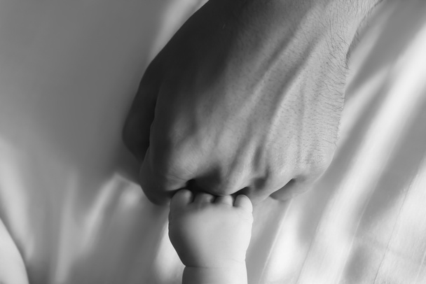 μαύρο και άσπρο φωτογραφία από τα χέρια του ο άνθρωπος και νήπιο γιος στο κρεβάτι  - Φωτογραφία, εικόνα