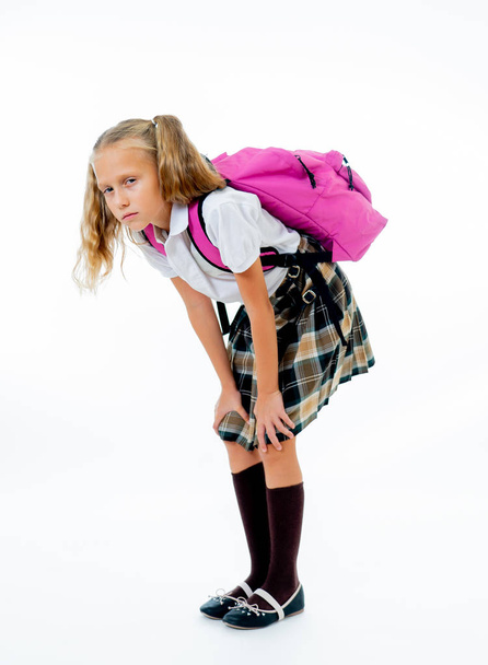 Young tired and sad cute school girl standing with a big heavy school bag on her back isolates on white background - Photo, image