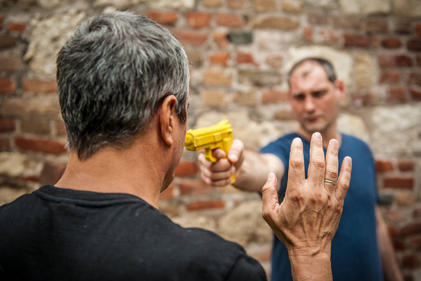 Robber with a gun attacks the victim in a abandoned part of the city. Gun point disarm training - Фото, изображение