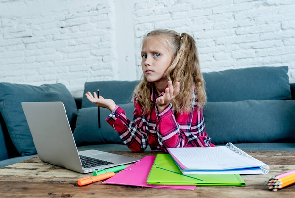 Cute elementary student feeling sad and confusing while doing difficult assignment with her laptop at home. Homework and children education concept. - Foto, immagini