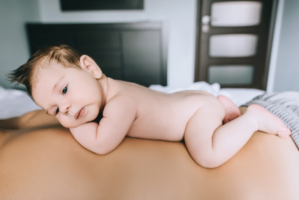 selective focus of infant boy laying on father back in bed at home - Φωτογραφία, εικόνα