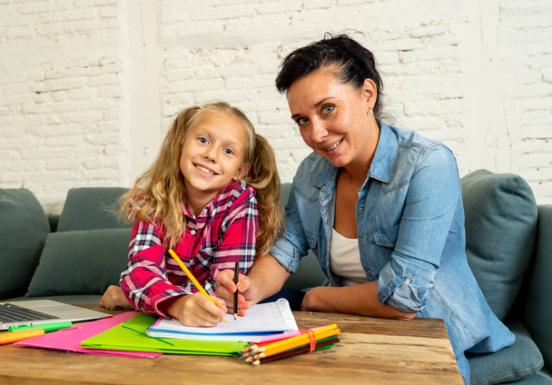 Beautiful mother helping her young blonde cute sweet girl doing homework at home. Homework parenting and education concept - Фото, изображение
