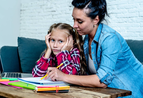 Patience mum with daughter unable to concentrate while doing homework sitting on sofa at home  - 写真・画像