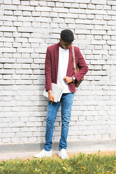 κομψό αφρικανική αμερικανική freelancer με έγγραφα και σακίδιο πλάτης δερμάτινο στέκεται κοντά σε λευκό τοίχο - Φωτογραφία, εικόνα