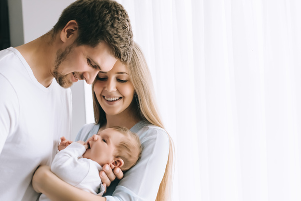 cheerful family carrying little baby boy in front of curtains at home - Photo, Image