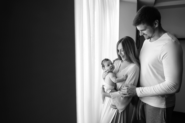 black and white picture of happy family carrying little baby boy in front of curtains at home - Foto, Imagem