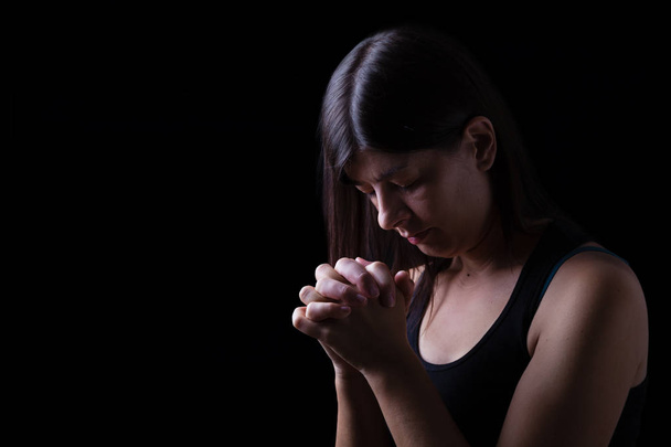 Uskollinen nainen rukoilee, kädet ristissä palvoen Jumalaa pää alaspäin ja silmät kiinni uskonnollisessa kiihkossa, mustalla taustalla. Uskonnon, uskon, rukouksen ja hengellisyyden käsite
. - Valokuva, kuva