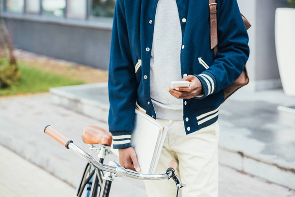 cropped view of stylish african american teleworker with documents using smartphone and standing near bike - Foto, Imagen