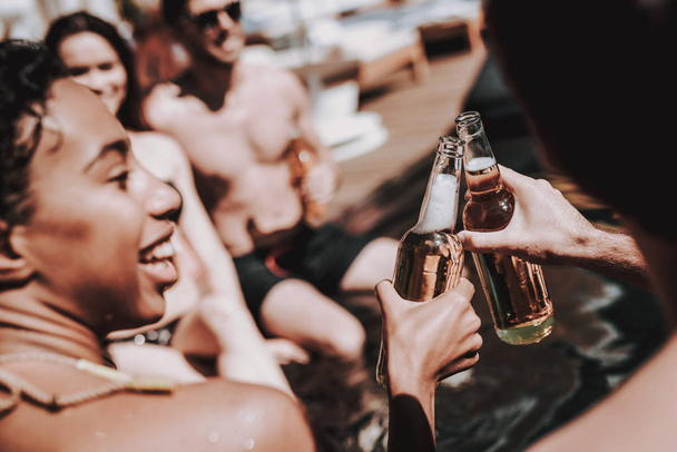 Young Friends with Alcoholic Drinks at Poolside. Group of Young Smiling People holding Bottles of Beer and having Fun at Poolside. Happy Friends Enoying Pool Party. Summer Vacation Concept - Фото, изображение