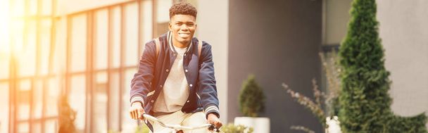homem americano africano alegre andar de bicicleta na cidade com luz solar
 - Foto, Imagem