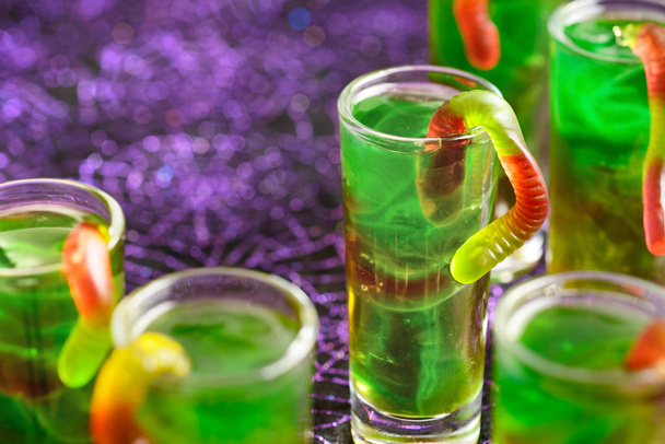 green Halloween jello shots with gummy worms on the purple background - Photo, image