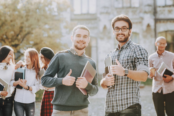 Thumbs Up. Guys. Books. Standing in University. Good Mood. Intelligence. Standing Together. Outside. Sunny Day. Students. Holding Friends. Happy. Students. Courtyard. Books. University. Knowledge. - 写真・画像