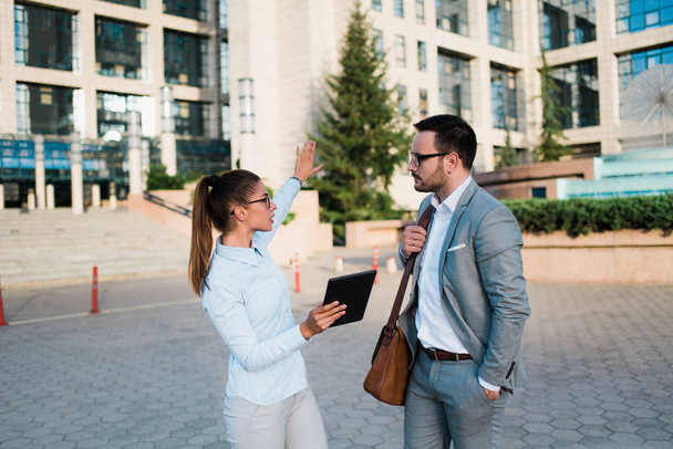 Young successful business people looking at business plans and charts, standing in front of a business building and talking. - Photo, Image