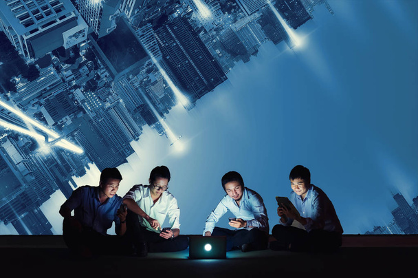 Asian business group using smartphone, tablet and laptop for working or social networks and wep site on high-rise rooftop. Business and technology concept. upside down cityscape. - Photo, Image