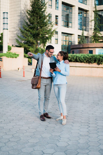 Joven hombre de negocios y mujer de negocios hablando de ideas de negocios utilizando tableta, de pie frente a un edificio de vidrio
.  - Foto, Imagen