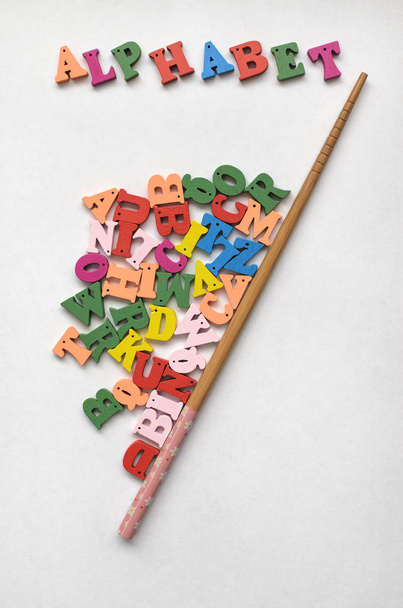 Lettere multicolori dell'alfabeto, l'alfabeto di iscrizione e un puntatore scolastico in legno su uno sfondo di legno
. - Foto, immagini