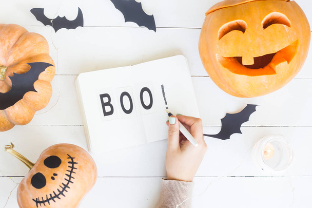 Boo - written in notebook among the decorations for Halloween - pumpkins and bats on a white wooden table. Top view, flat lay - Photo, image