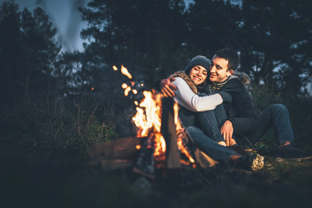 Pretty young couple relaxing near bonfire in the forest at evening time - Foto, afbeelding