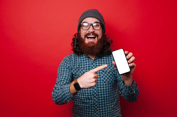 Portrét vzrušený vousatý muž ukázal na prázdnou obrazovku na smartphone - Fotografie, Obrázek