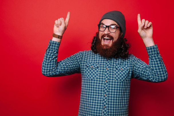 Retrato de hombre feliz con barba apuntando hacia arriba sobre fondo rojo
 - Foto, imagen