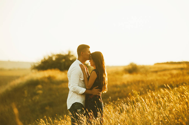 Jovem casal apaixonado em um campo ao pôr-do-sol. Homem kisinig mulher na testa
. - Foto, Imagem