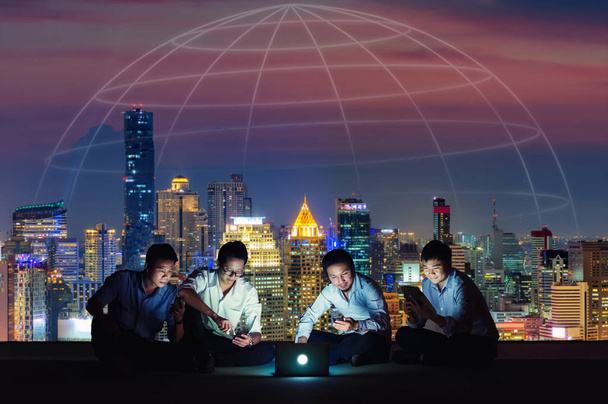 Asian business group in casual suits using smartphone, tablet and laptop for working or playing social networks and wep site on high-rise rooftop sites. Business and technology concept - Photo, Image