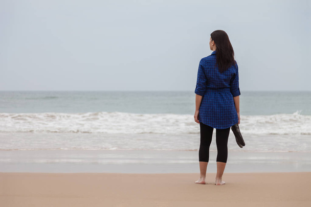 Μοναχικός και μελαγχολικός γυναίκα να στέκεται μπροστά στη θάλασσα, σε μια ερημική παραλία για μια ημέρα του φθινοπώρου. - Φωτογραφία, εικόνα