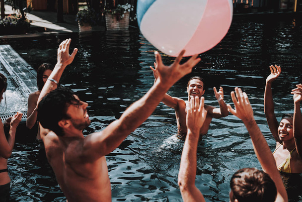 Gruppe junger lächelnder Freunde, die sich im Pool vergnügen. Junge fröhliche Menschen spielen im Freibad zusammen mit bunten Strandbällen. Freunde auf Poolparty. Sommerferienkonzept - Foto, Bild