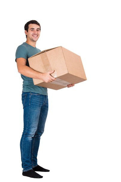 Full length portrait of smiling young man carrying a big cardboard box, worder shipping isolated over white background. - Foto, afbeelding