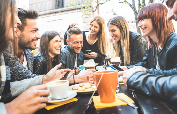 Happy friends talking and having fun with mobile smart phones at restaurant drinking cappuccino and hot tea - Young people together at cafeteria - Friendship concept with men and women at coffee bar - 写真・画像
