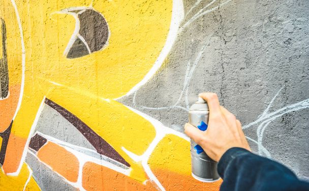 Detail of street artist painting colorful graffiti on public wall - Modern art concept with urban guy drawing live murales with multi color aerosol spray - Vintage filter with focus on yellow paint - 写真・画像