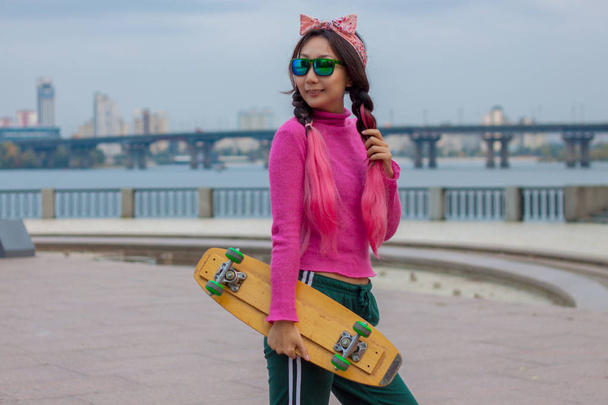 Helder gekleed meisje met skateboard in de stad - Foto, afbeelding