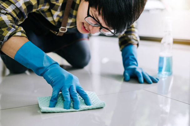 Husband housekeeping and cleaning concept, Happy young man in blue rubber gloves wiping dust using a spray and a duster while cleaning on floor at home. - Foto, immagini