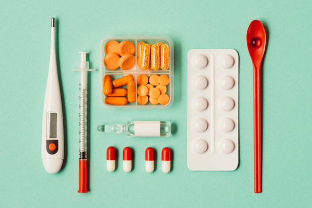 bovenaanzicht van verschillende medicijnen, spuit en thermometer op groen - Foto, afbeelding