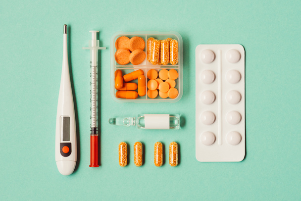 bovenaanzicht van thermometer, injectiespuit, ampul met geneeskunde, blister pack en pillen op groen - Foto, afbeelding