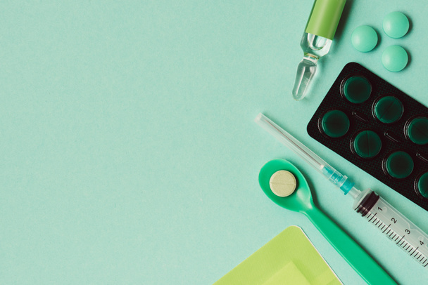 top view of ampoule with medicine, blister pack, pills and syringe on green background - Photo, image