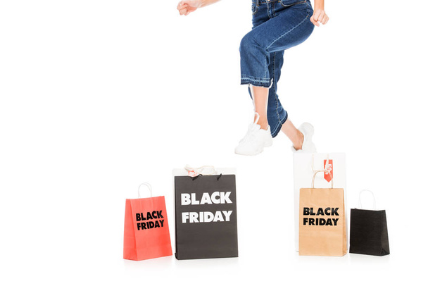 cropped view of girl jumping near shopping bags with black friday sale signs isolated on white - Fotó, kép