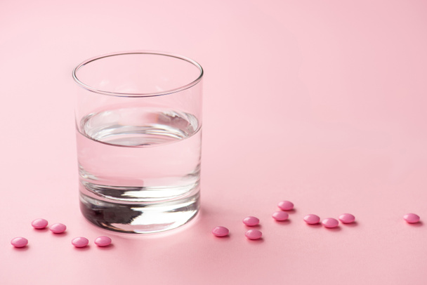 close-up view of glass of water and medical tablets on pink   - Fotografie, Obrázek