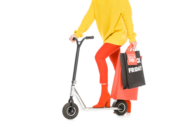 cropped view of girl riding scooter with shopping bags for black friday isolated on white - Foto, Imagen