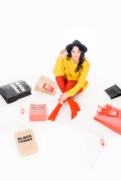 fashionable female shopaholic sitting at shopping bags on black friday sale, isolated on white - Fotó, kép