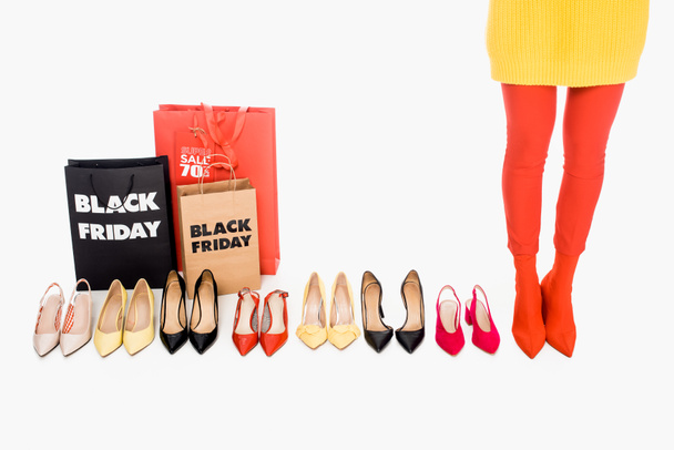 partial view of woman, shopping bags with black friday inscription and stylish female footwear isolated on white - Fotó, kép