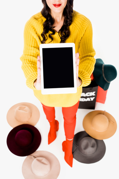 fashionable woman showing tablet with blank screen in hands, hats and shopping bags around isolated on white - Photo, Image
