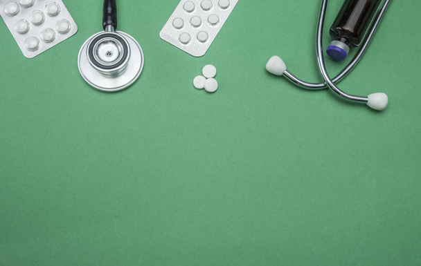 Stethoscope And tablets of pills isolated on a green background, conceptual image - Fotoğraf, Görsel