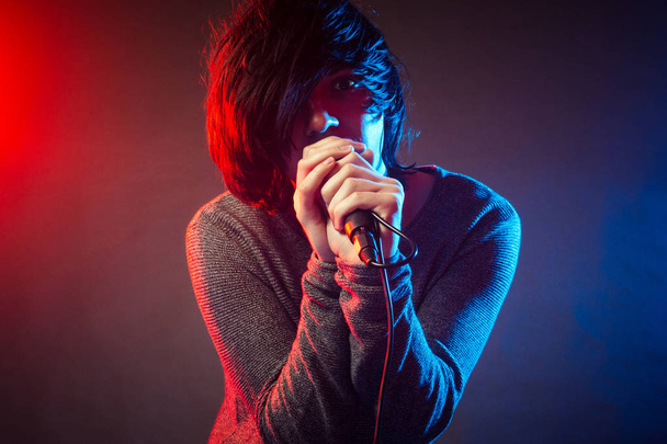 The young singer or vocalist in emo style is singing on concert on background of red and blue concert lights. - Foto, imagen