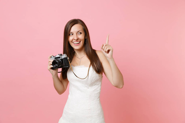 Šťastná nevěsta žena ve svatebních šatech ukazující ukazováček se drží retro vinobraní fotoaparát volba zaměstnanci fotograf izolované na růžovém pozadí. Svatební seznam. Organizace oslavy - Fotografie, Obrázek