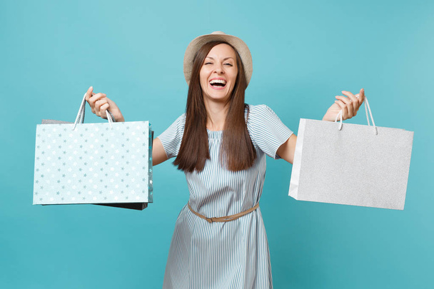 Portrait excited smiling beautiful caucasian woman in summer dress, straw hat holding packages bags with purchases after shopping isolated on blue pastel background. Copy space for advertisement - Foto, Bild