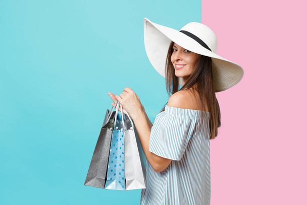 Portrait fashionable elegant fashion beautiful caucasian woman in summer dress, white large wide brim sun hat holding packages bags with purchases after shopping isolated on blue pastel background - Фото, изображение